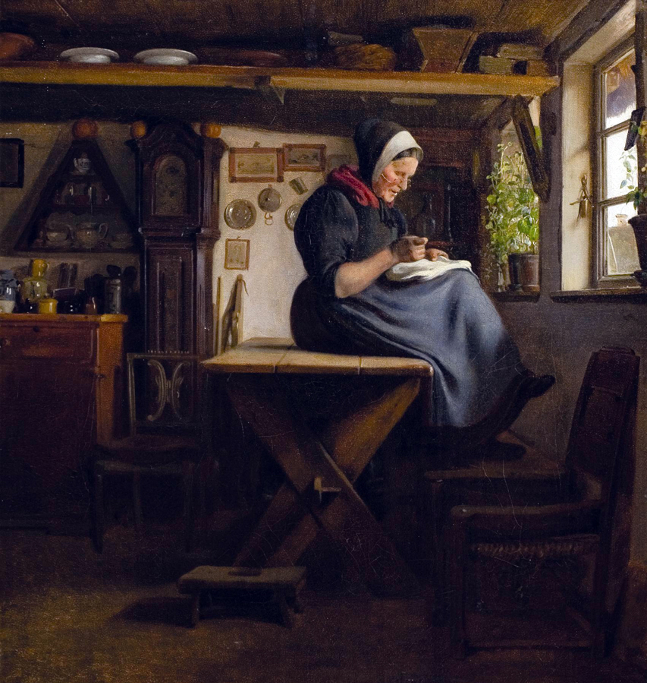 Hedebokvinde der sidder på spisebordet ved vinduet og syr på et hvidt stykke stof